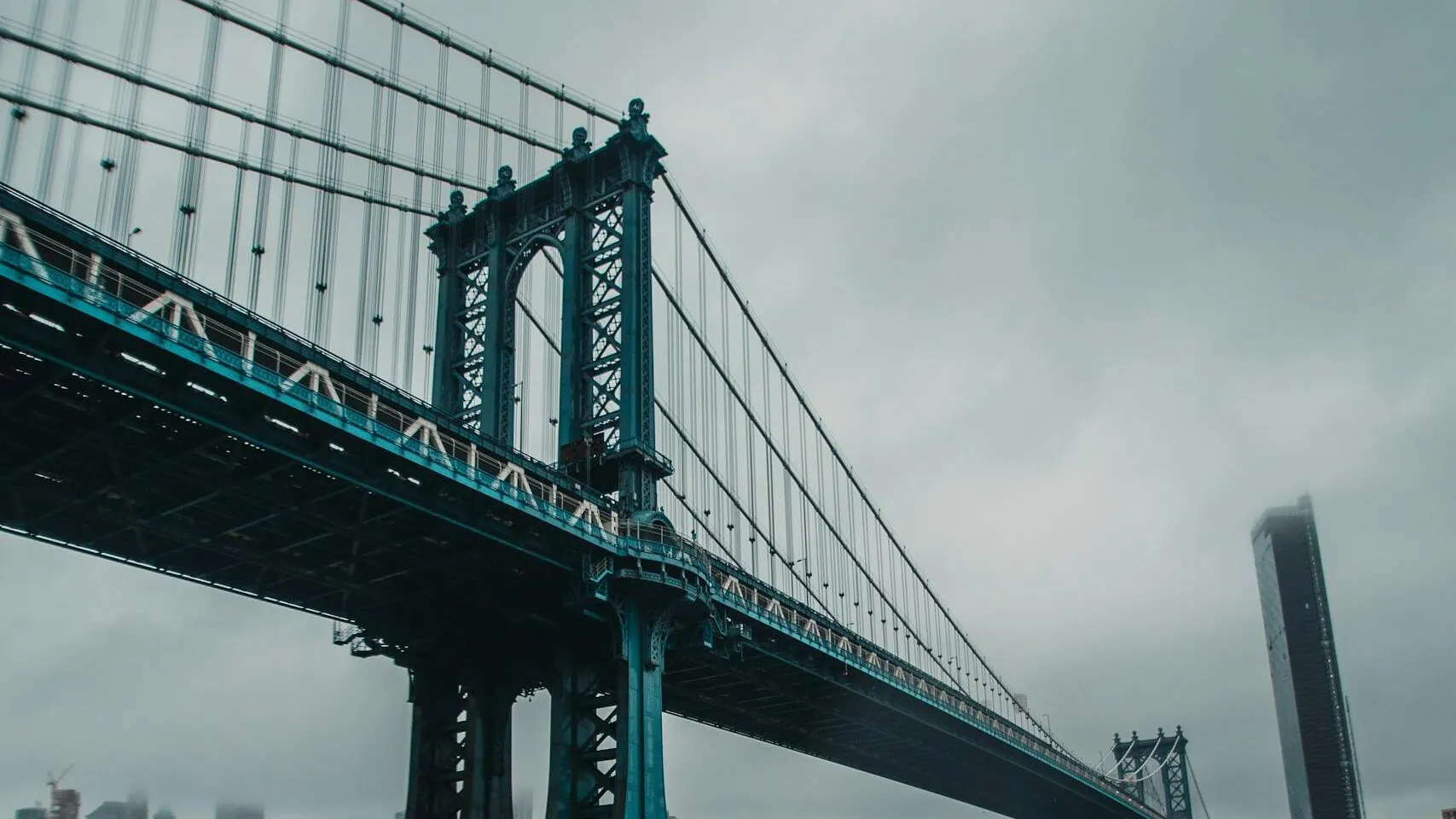 A cloudy day view of the iconic Manhattan Bridge spanning the East River in New York City.