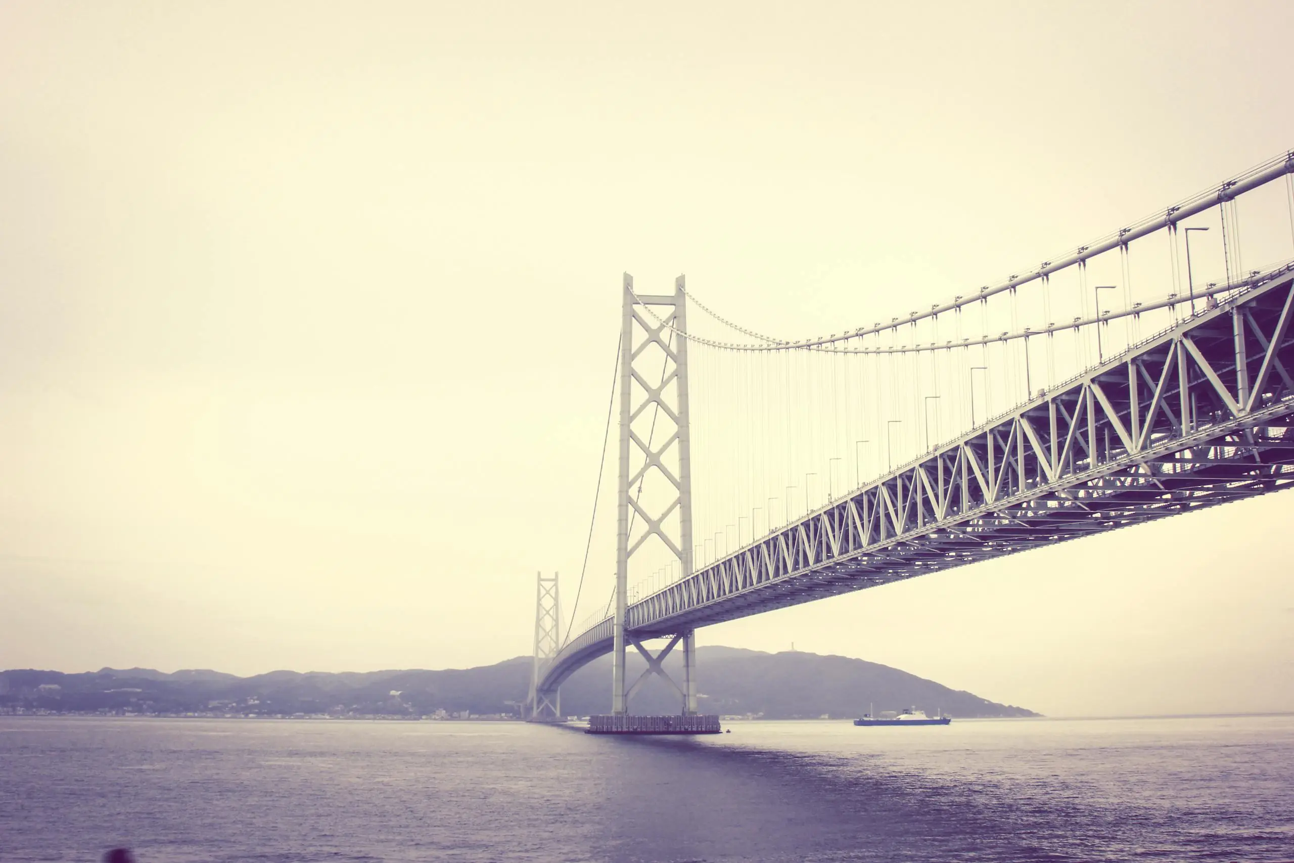 A stunning view of a suspension bridge spanning the sea with a hazy backdrop.